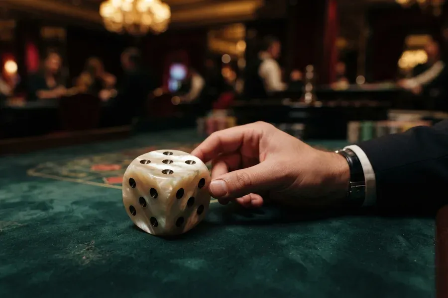 A hand rests beside a large ivory-colored die on a green felt table.