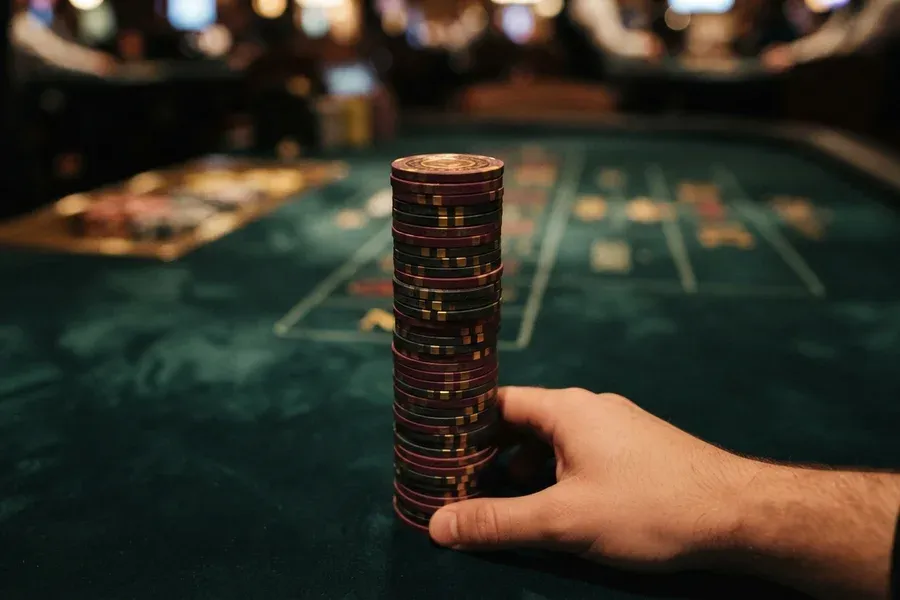 A hand steadies a tall stack of poker chips on a green table.